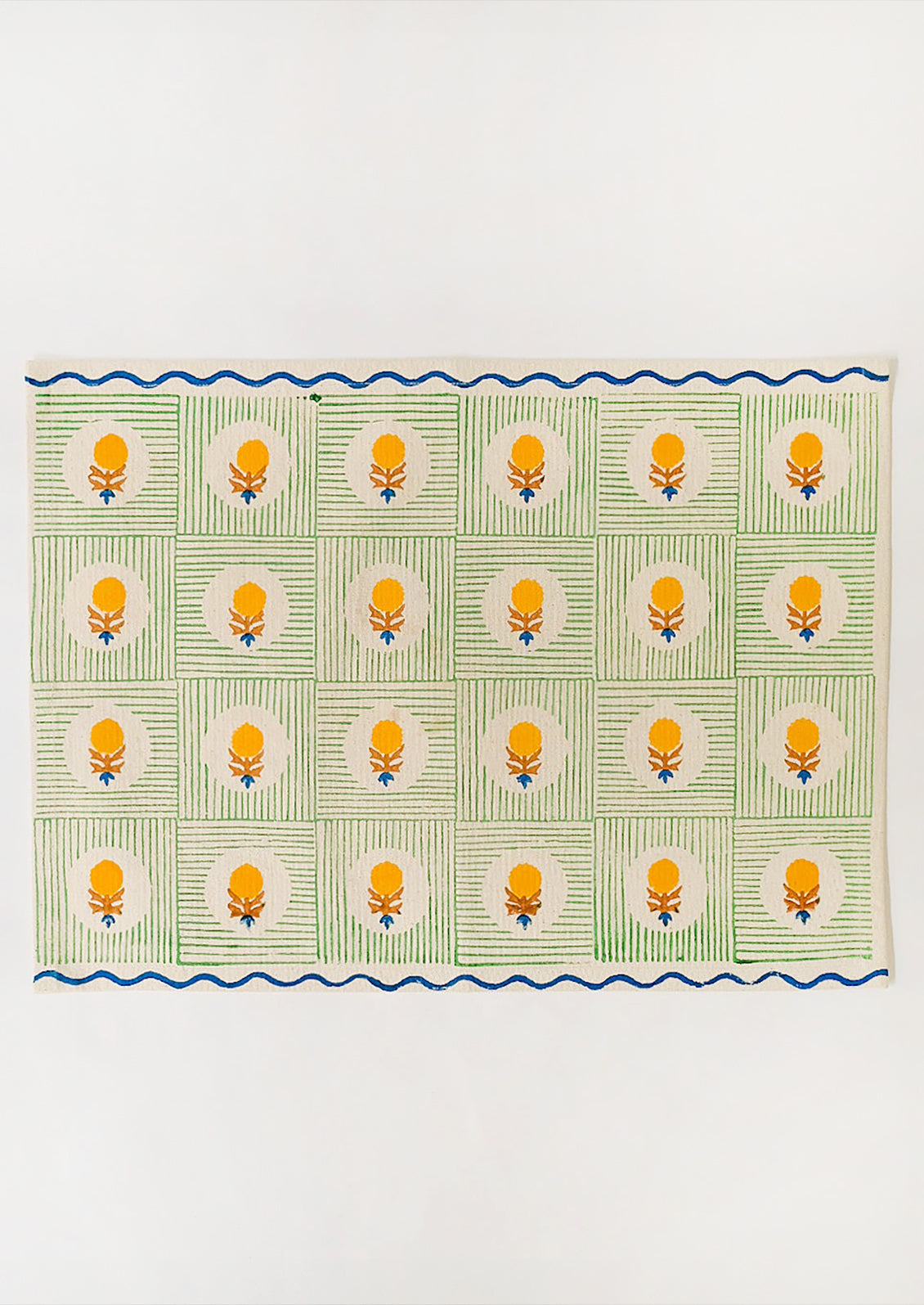 A block printed placemat in natural linen with green squares, yellow floral and blue wavy trim.