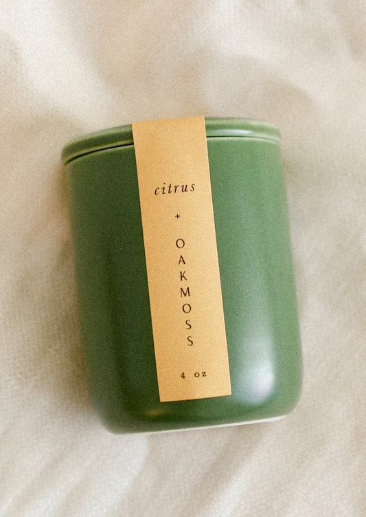 A small candle in lidded green ceramic jar in Citrus and Oakmoss scent.