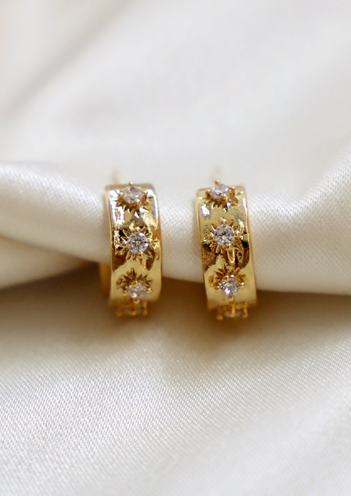 A pair of small gold hoop earrings with raised crystal starbust pattern.