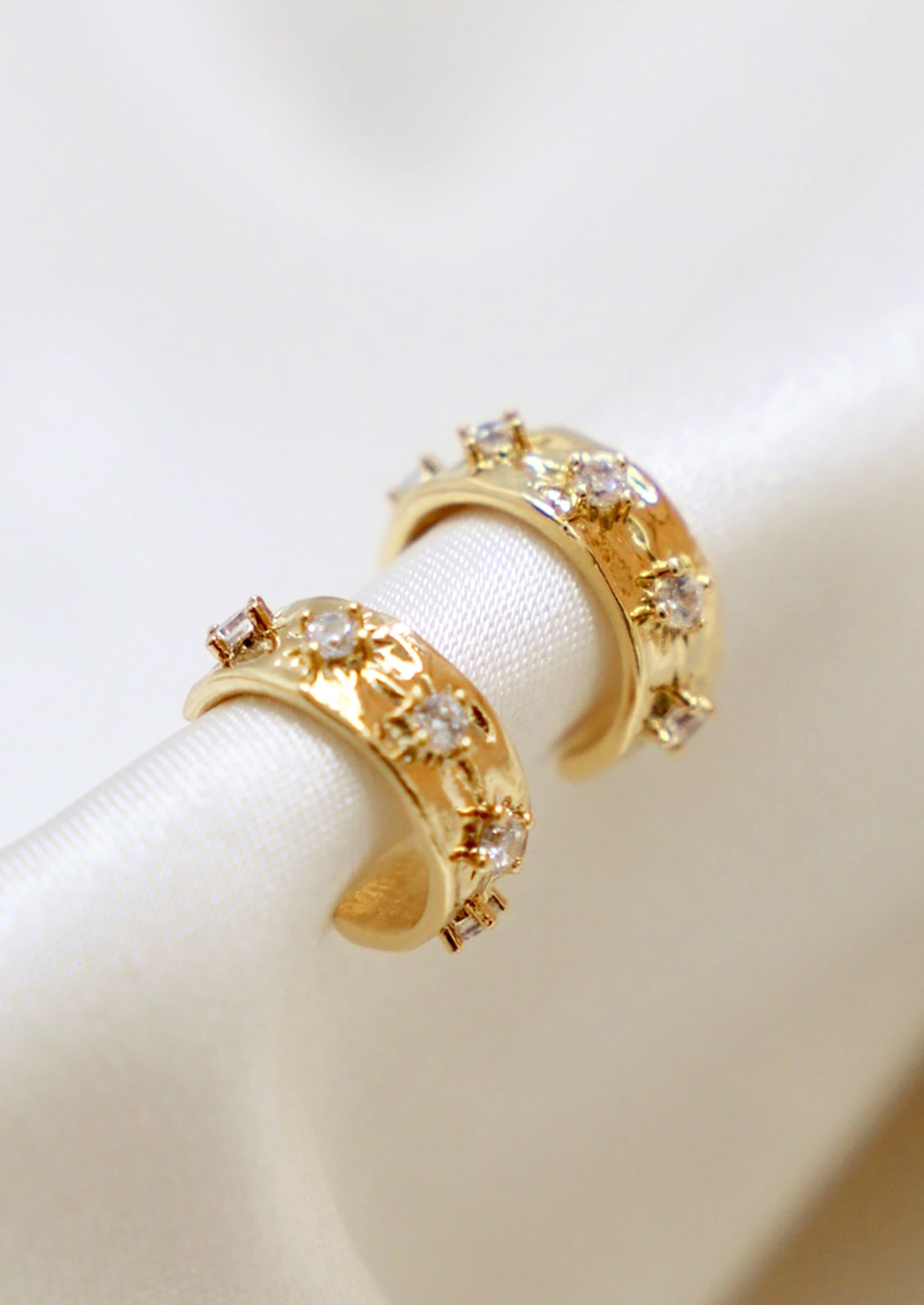 A pair of small gold hoop earrings with raised crystal starbust pattern.