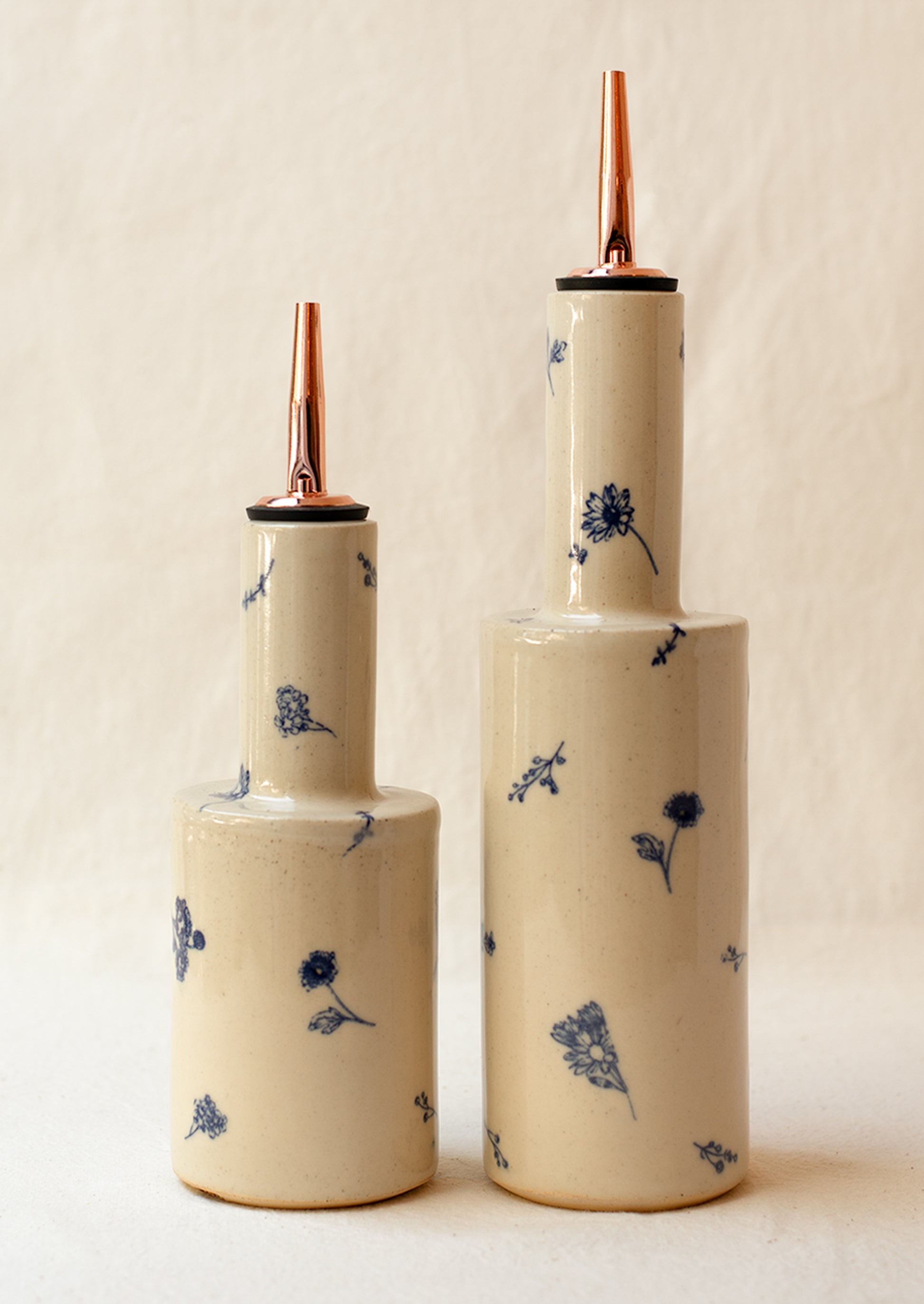 A pair of short and tall ceramic pouring bottles with blue floral pattern.