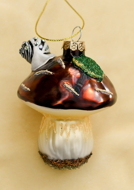 A glass ornament of brown mushroom with snail and leaf on top.