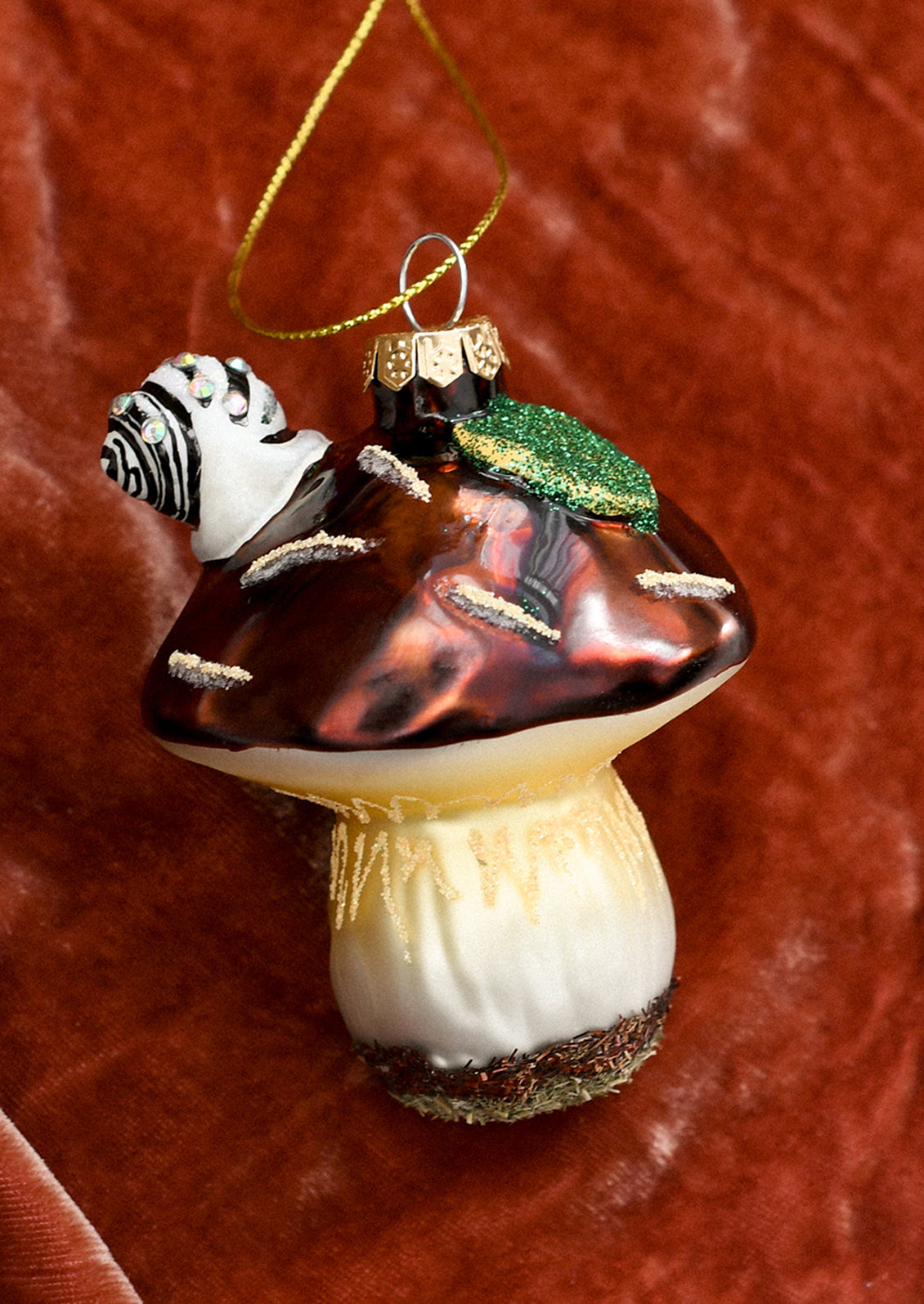 A glass ornament of brown mushroom with snail and leaf on top.