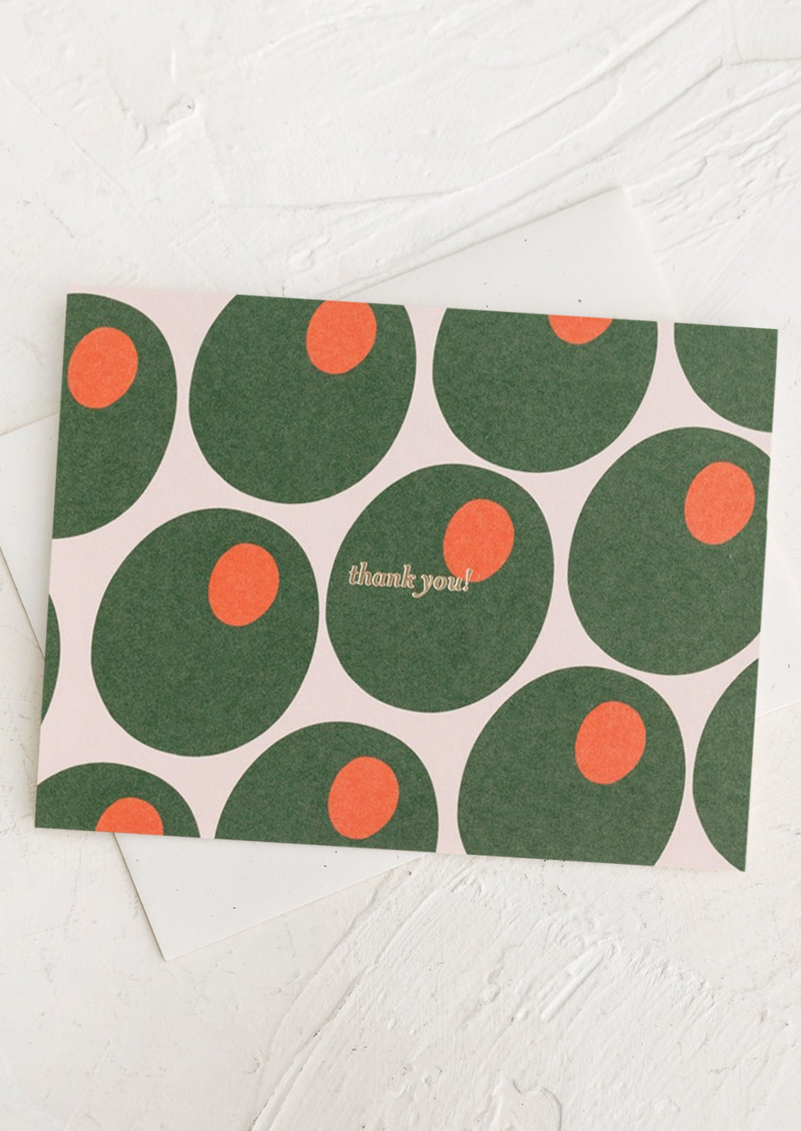 A greeting card with red and green olive print, gold lettering reads "Thank you!".