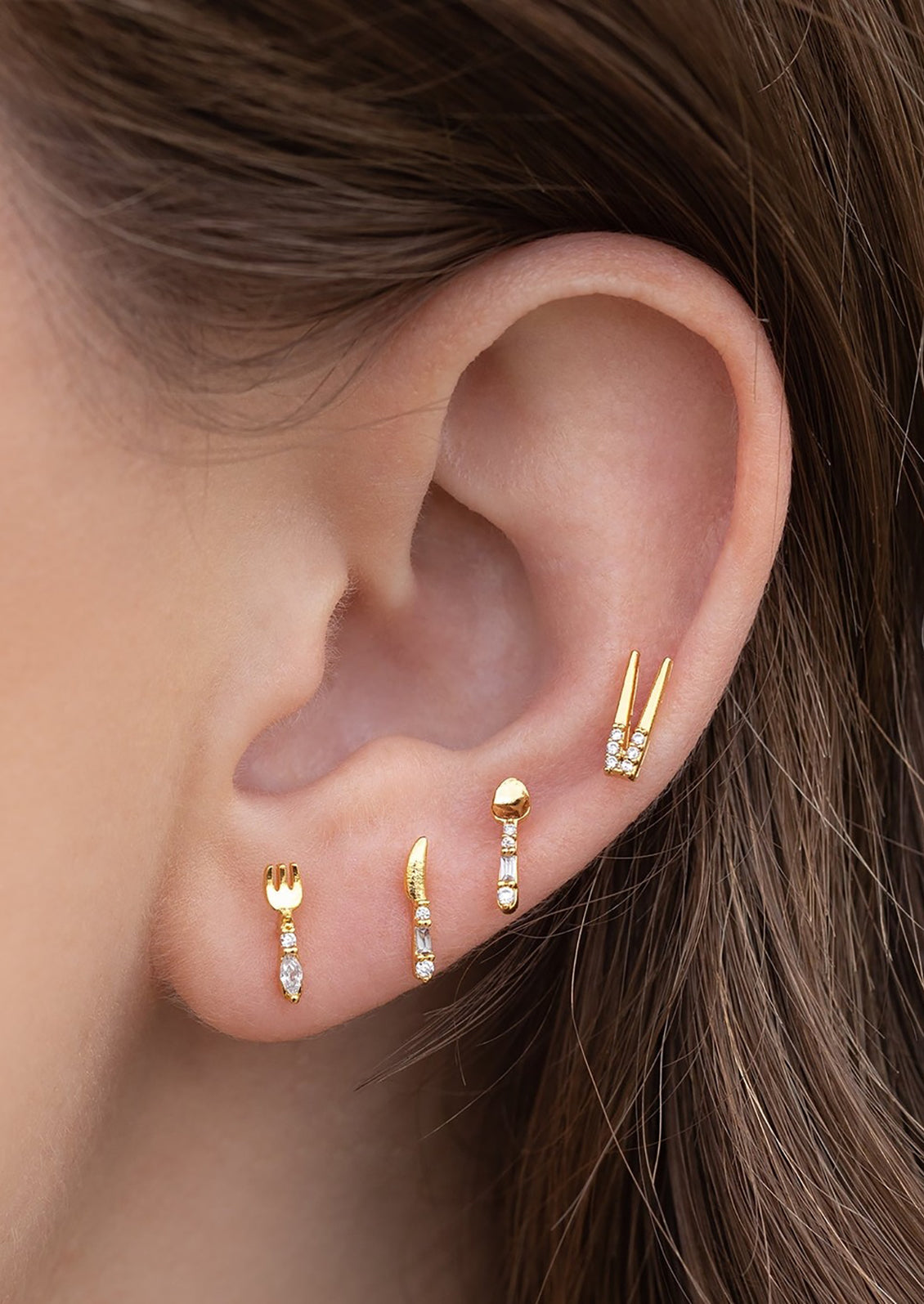 A set of four stud earrings in shape of chopsticks, fork, spoon, and knife.