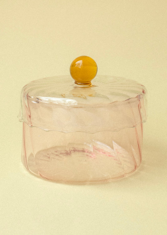 A pink tinted glass jar with yellow knob on lid.