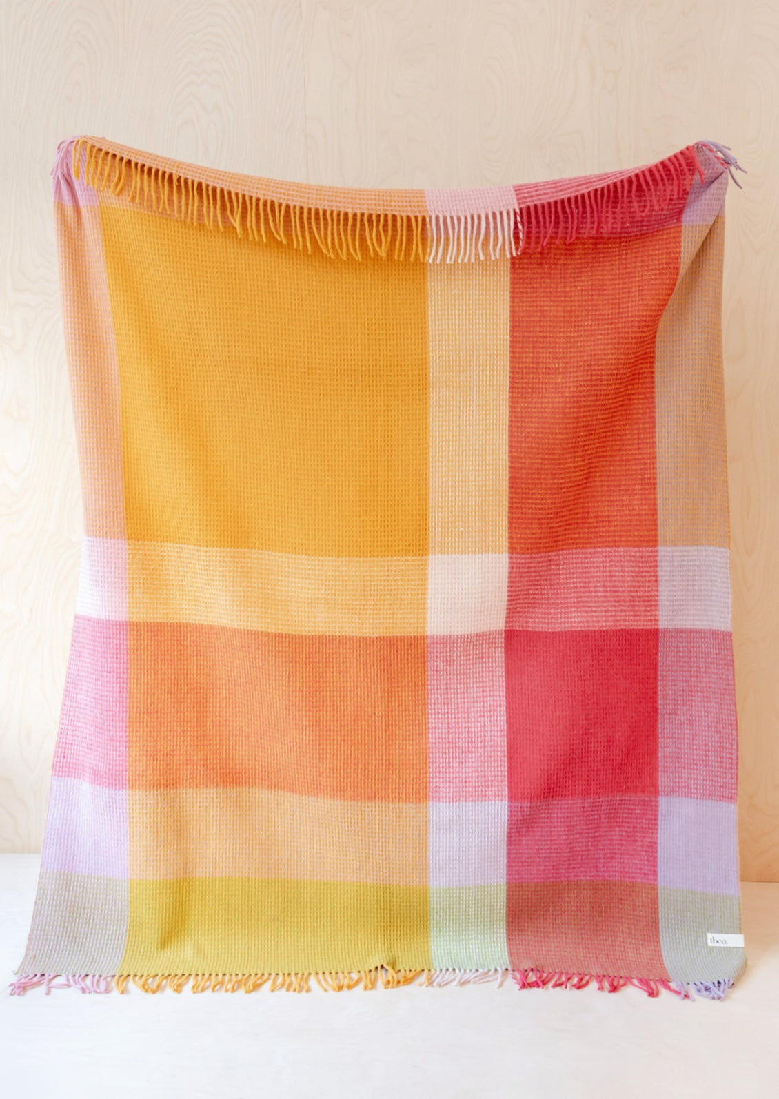 A colorblock large check patterned throw in magenta, orange, yellow and lavender tones.