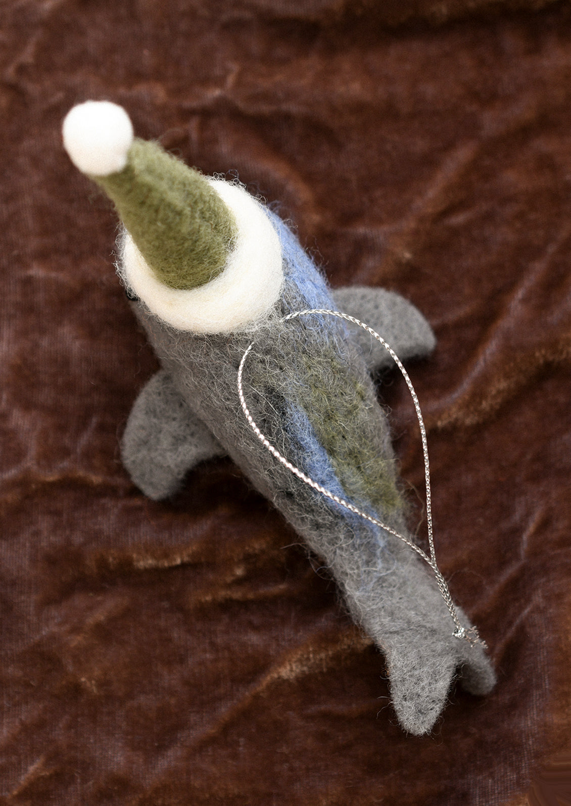 A felted wool ornament of whale in green party hat.