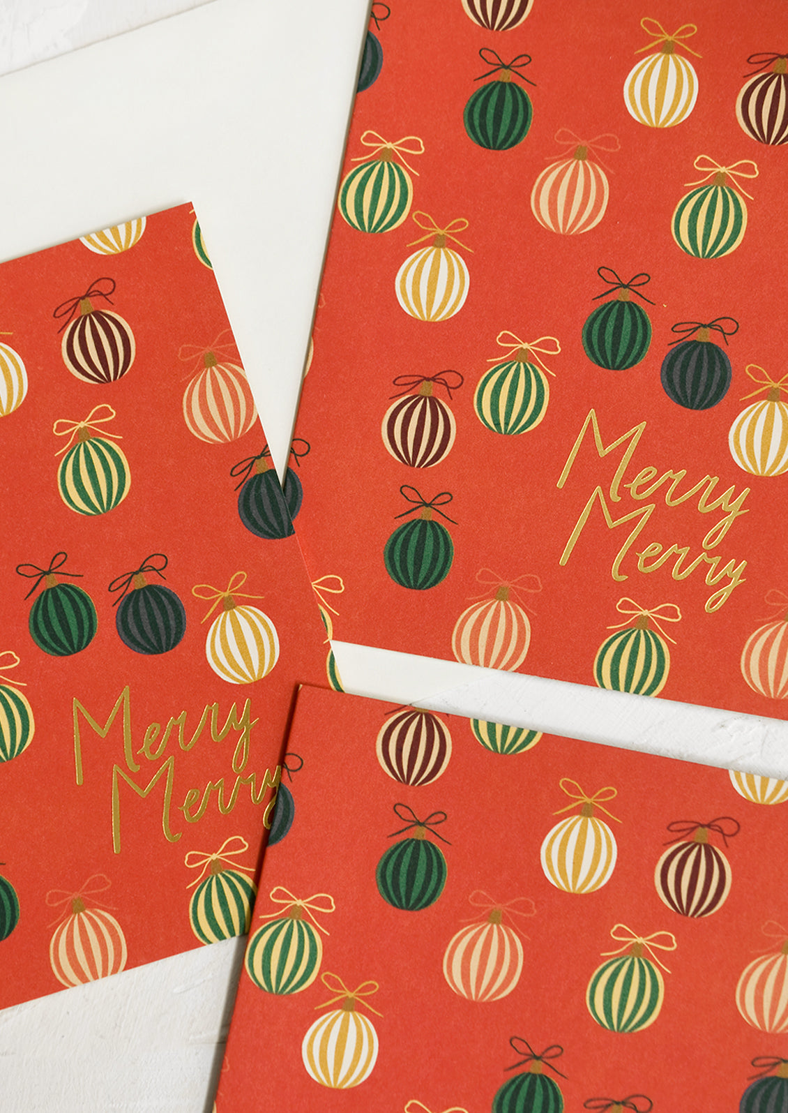 A set of red greeting cards with green ornament print, gold lettering reads "merry merry".