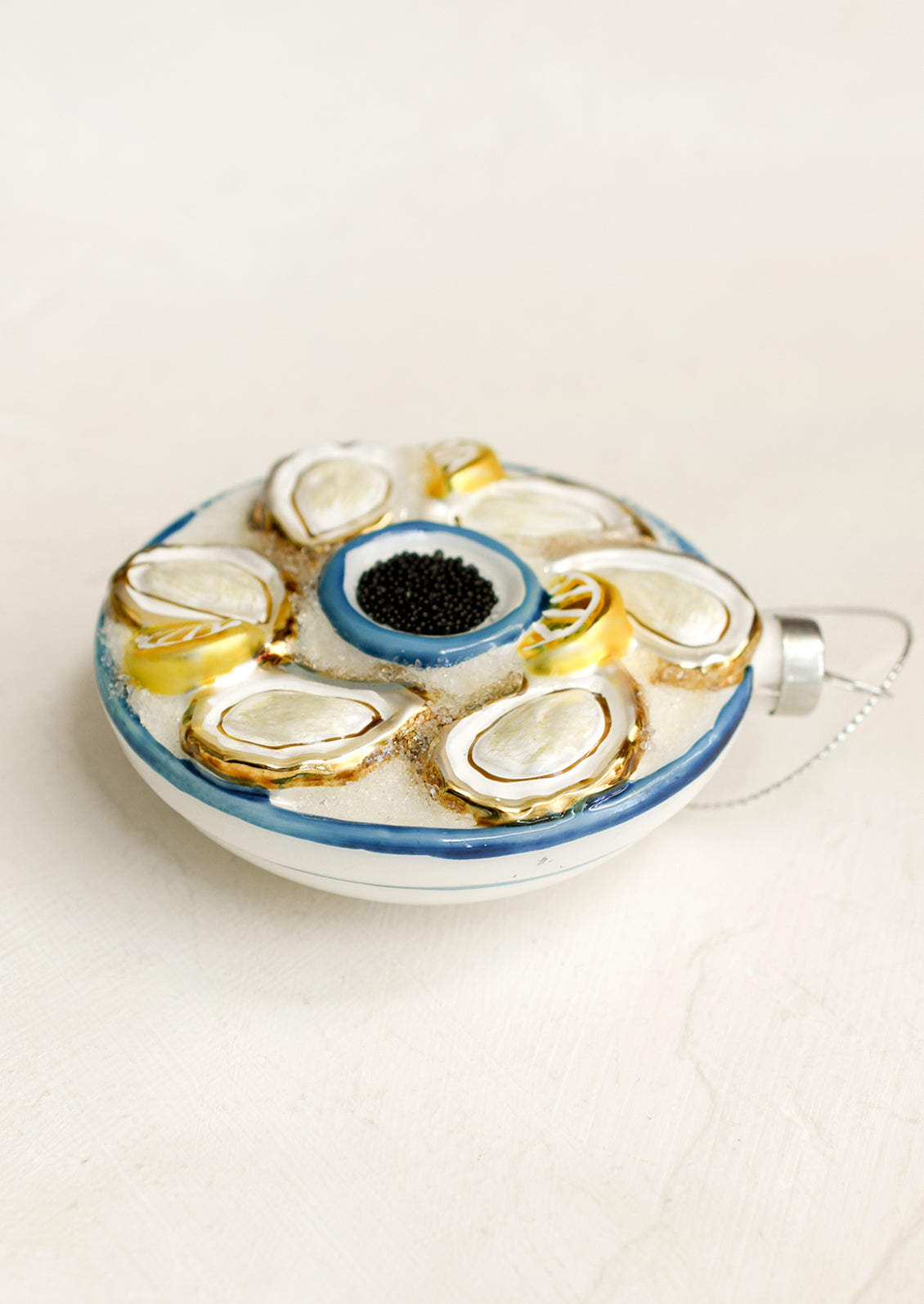 A round glass ornament depicting a tray of oysters, lemons and black caviar.