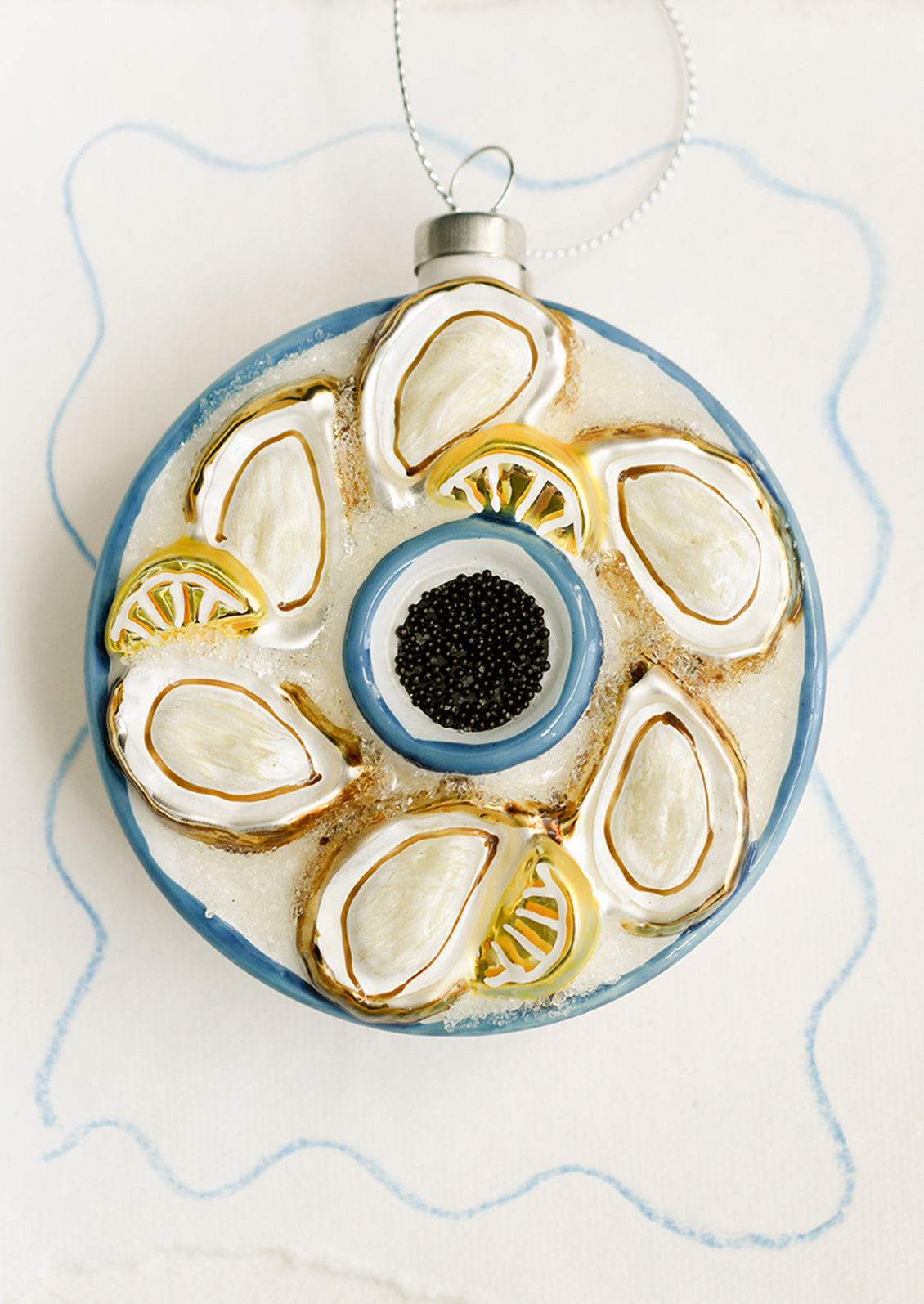 A round glass ornament depicting a tray of oysters, lemons and black caviar.