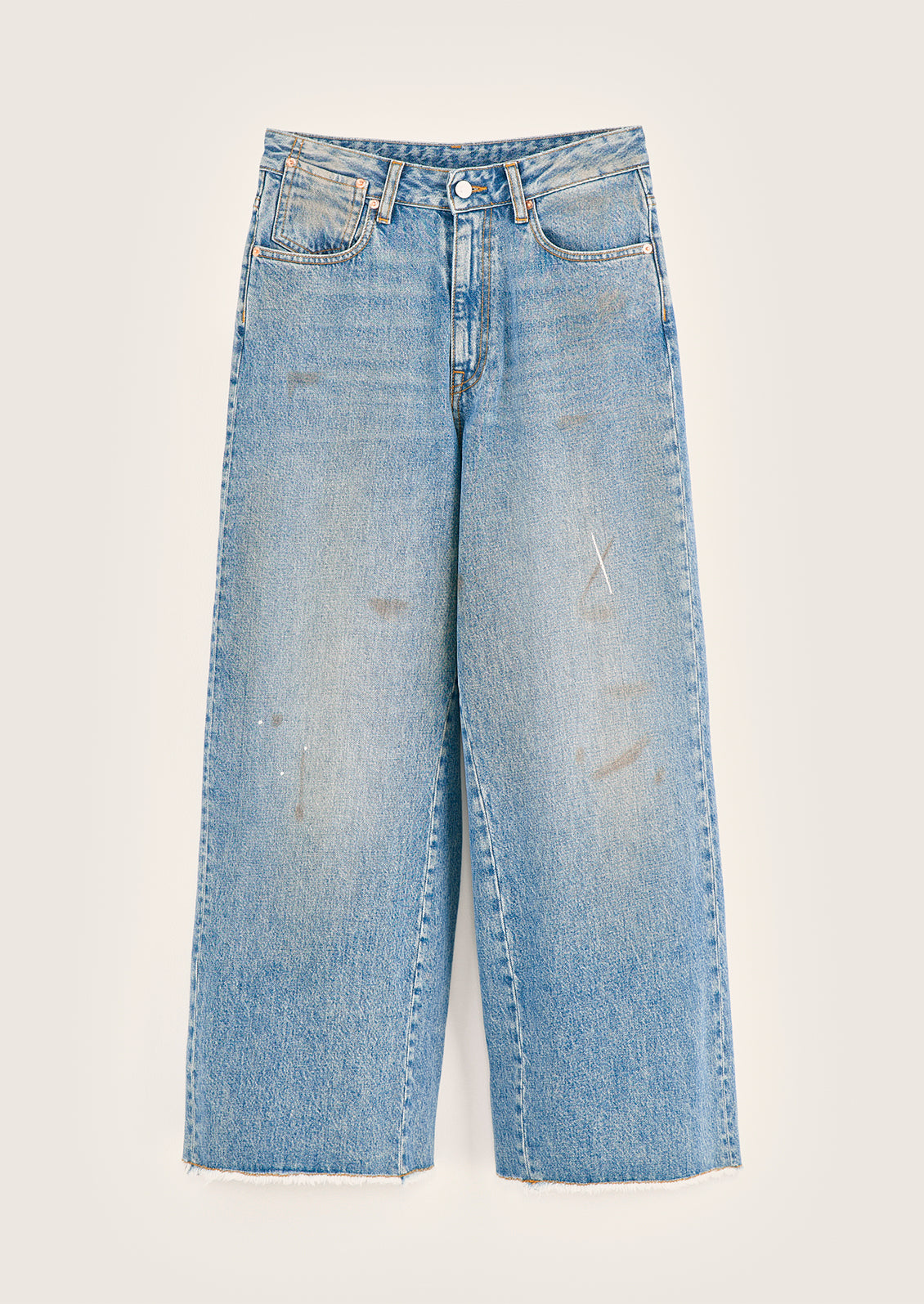 A pair of wide leg jeans in medium blue wash with dirt and paint marks.