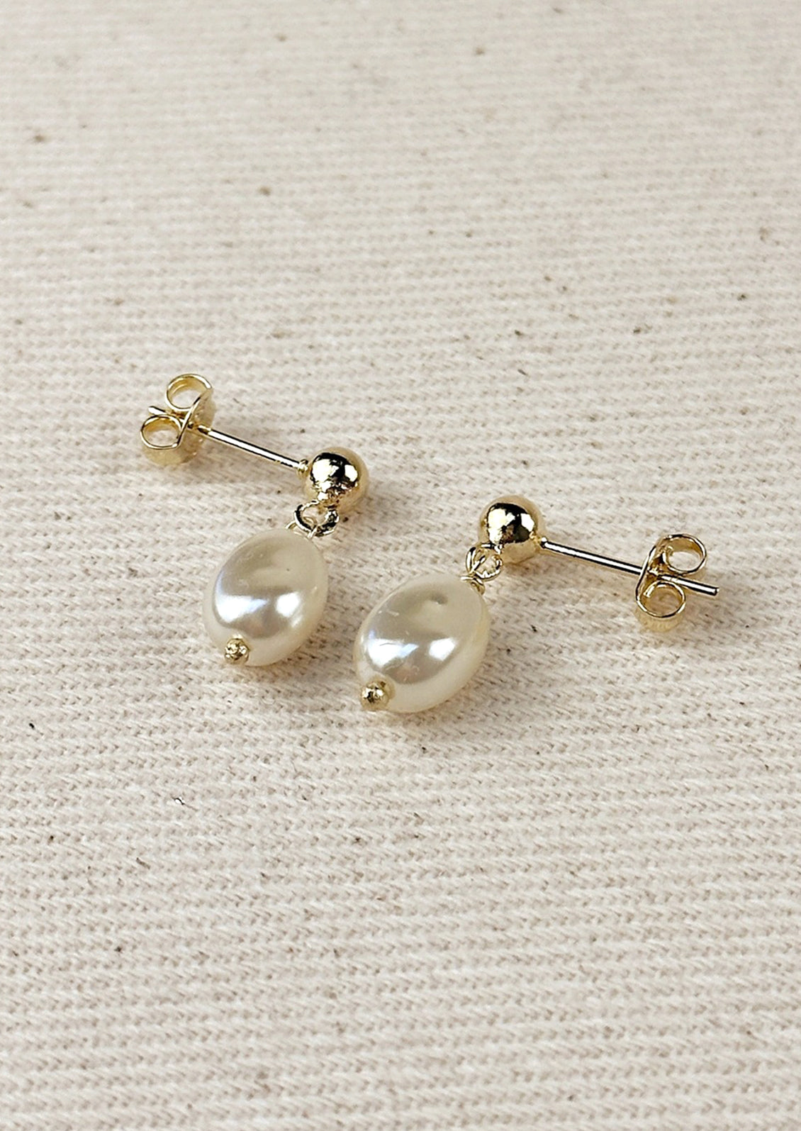 A pair of earrings with round ball post in gold with single pearl bead.