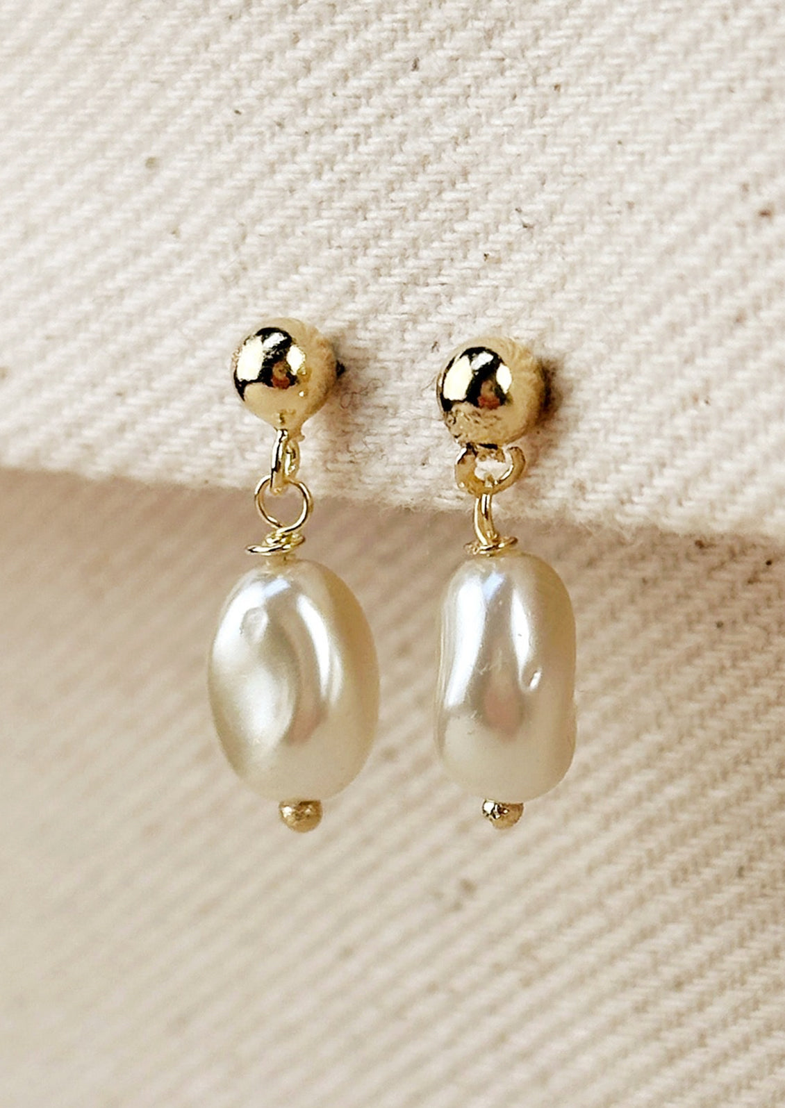 A pair of earrings with round ball post in gold with single pearl bead.