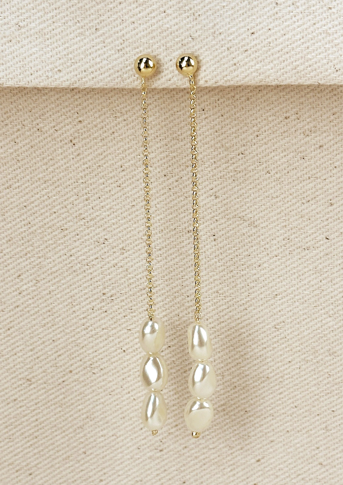 A pearl of gold dangling drop earrings with three pearl beads at bottom.