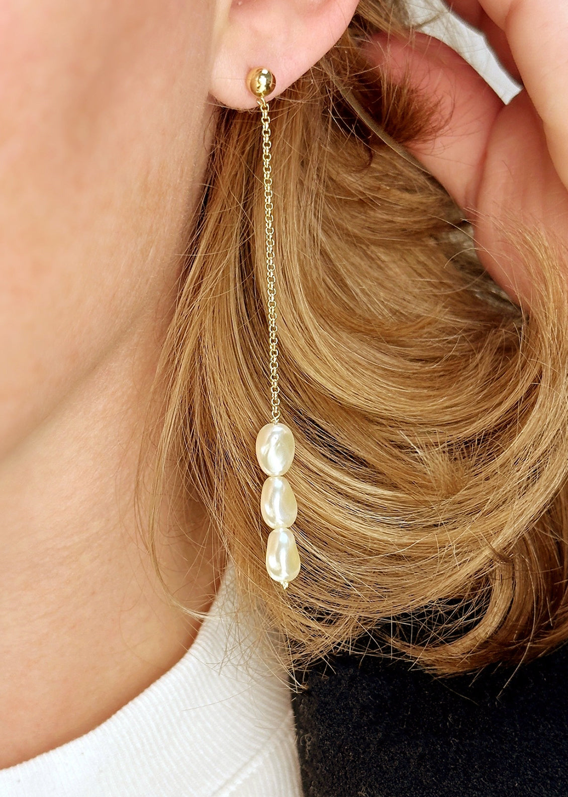 A pearl of gold dangling drop earrings with three pearl beads at bottom.