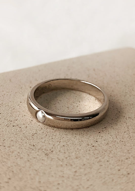 A silver ring with single inset pearl detail.