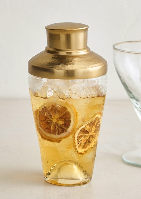 A small cocktail shaker in hammered glass with brass lid.