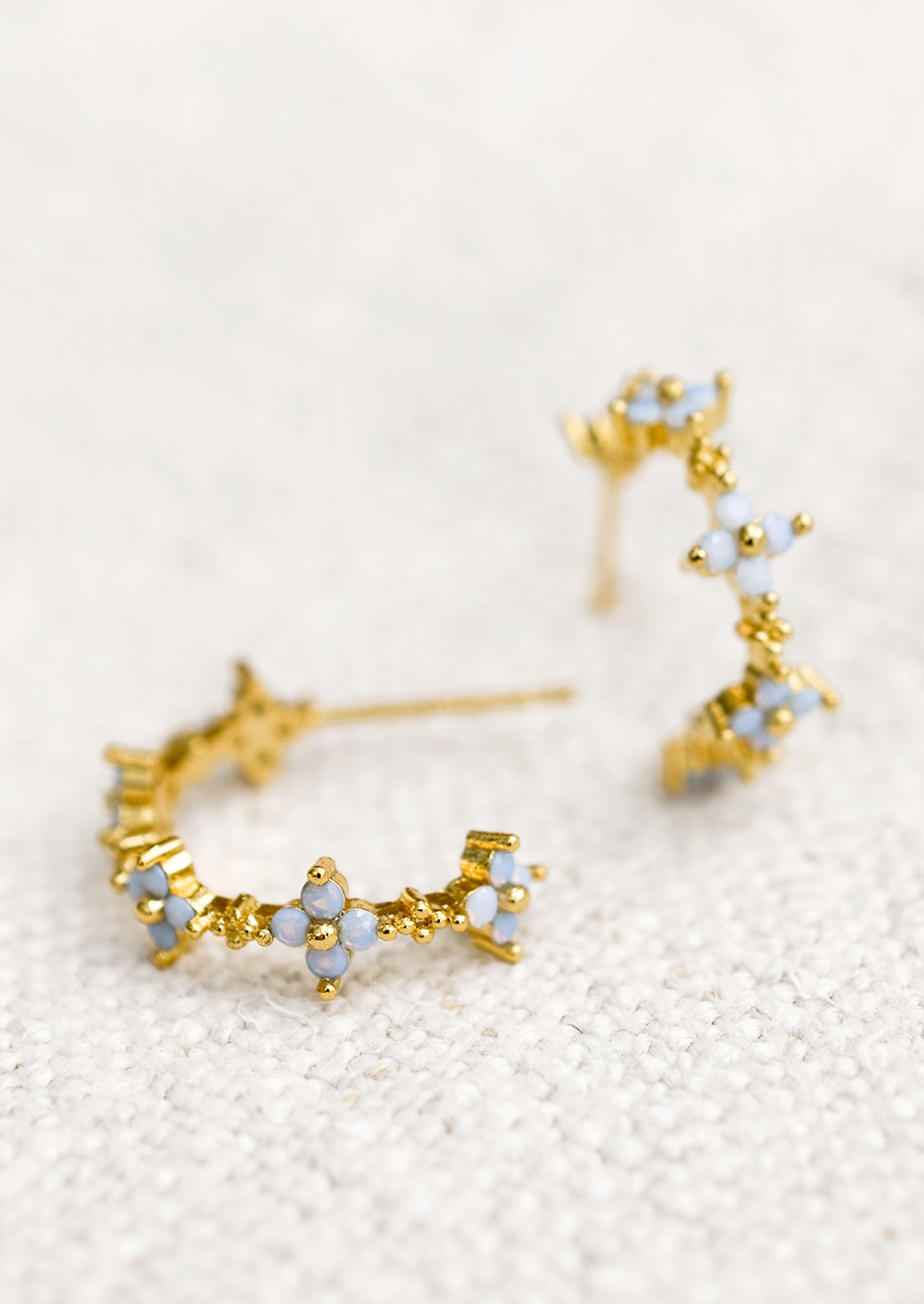 A pair of gold hoop earrings with periwinkle opal blue flowers.