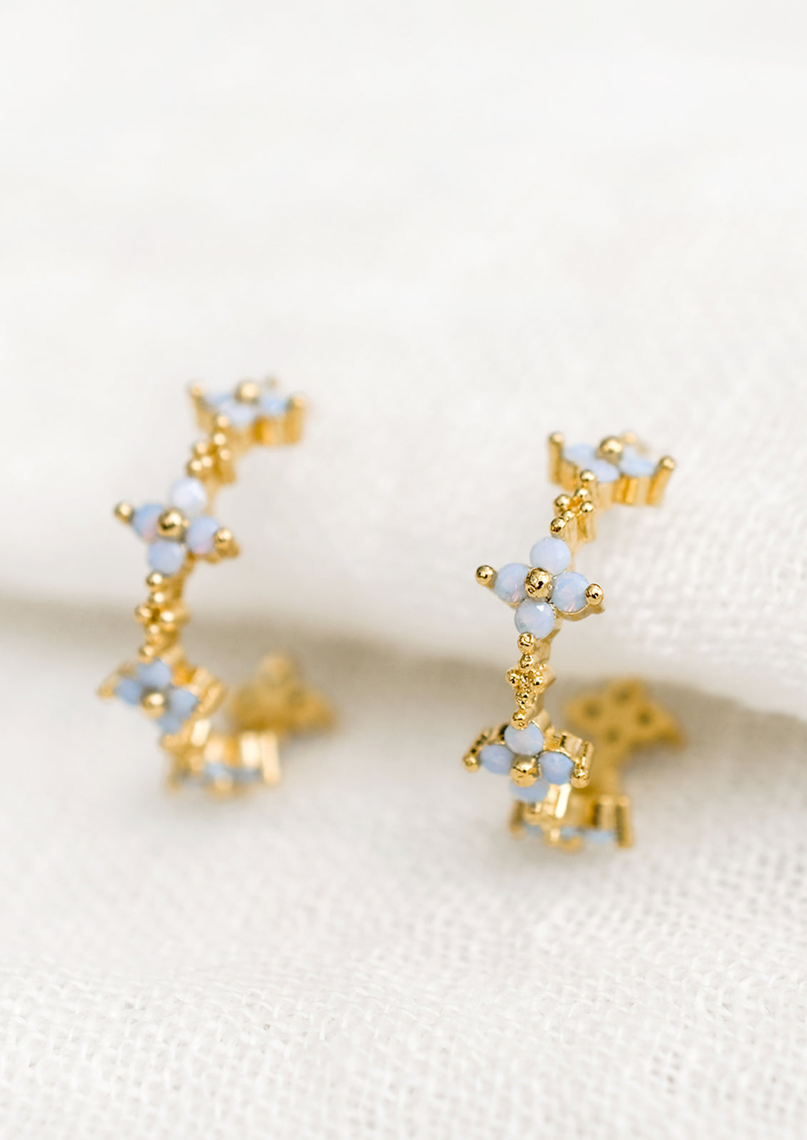 A pair of gold hoop earrings with periwinkle opal blue flowers.