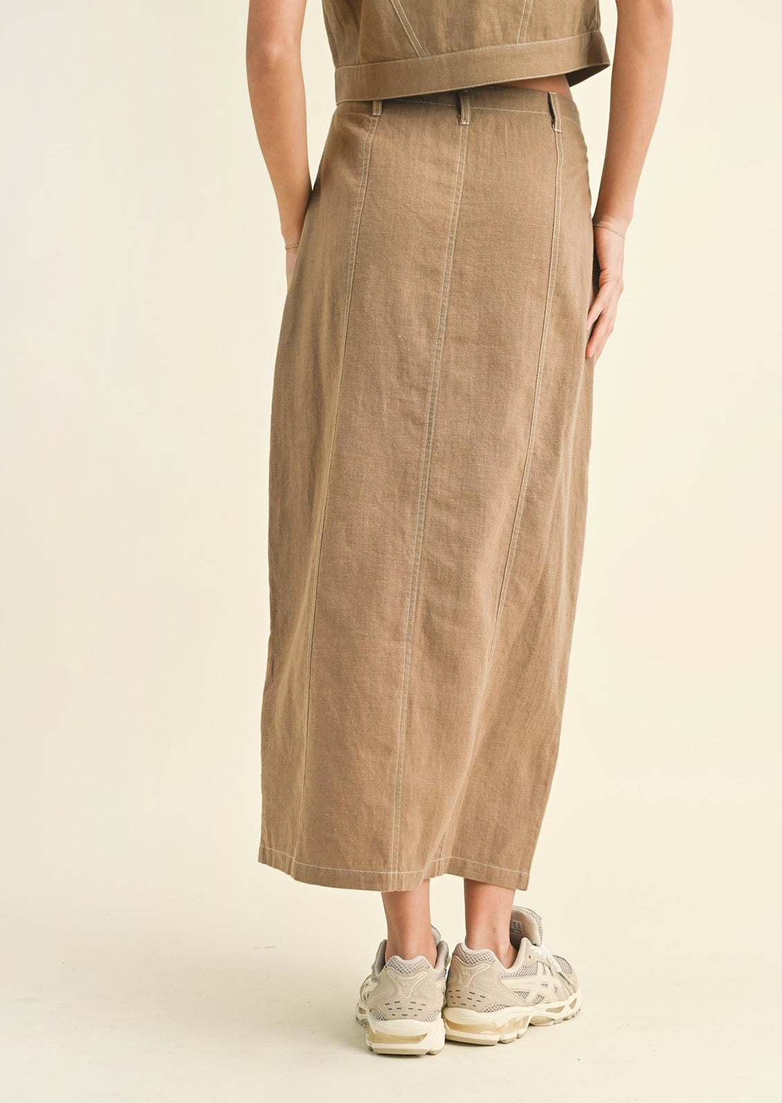 Woman wearing tan cotton midi skirt, seen from behind. 