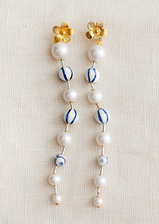 A pair of long dangling bead earrings in round pearl and blue striped ceramic, with gold flower post.