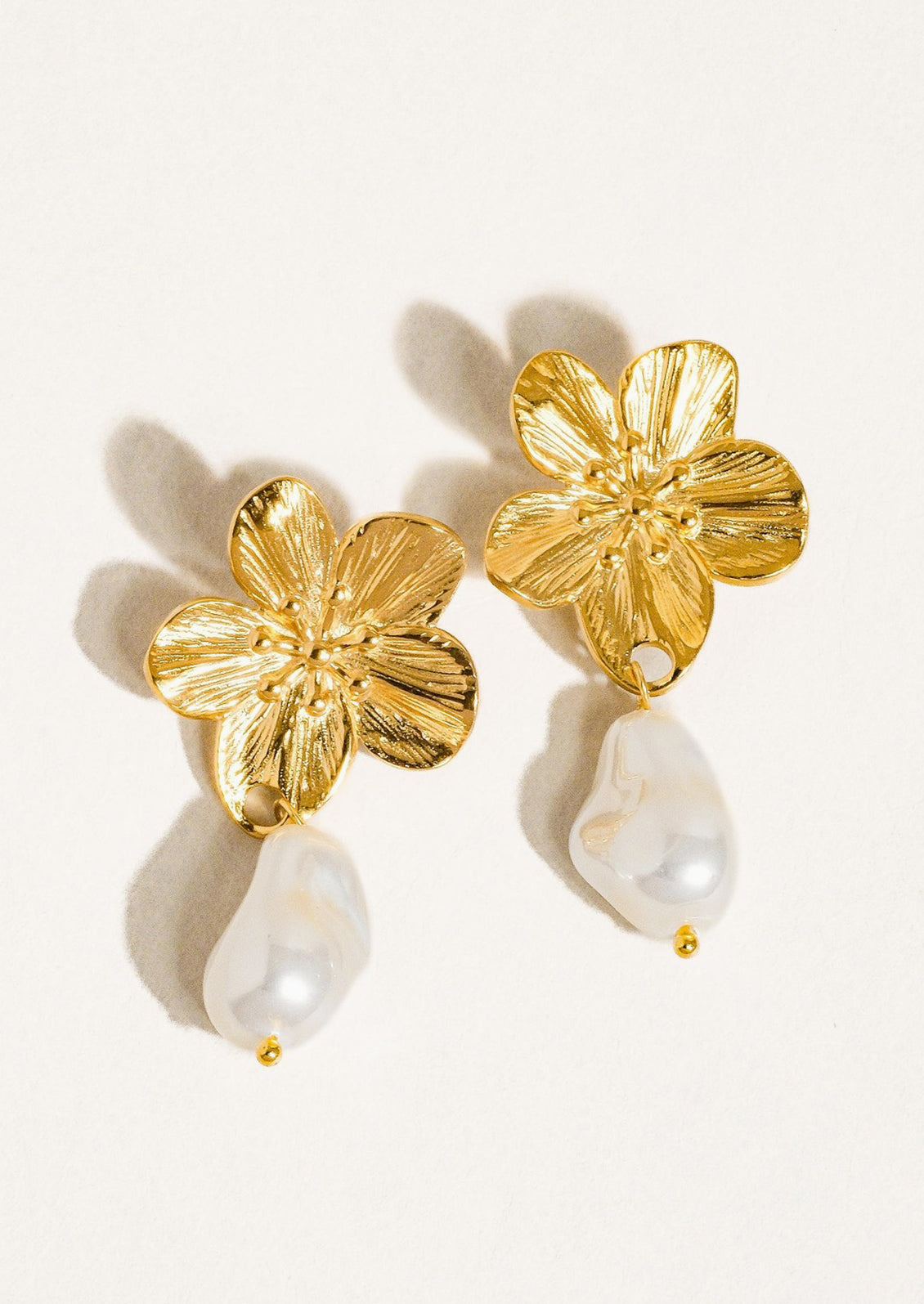 A pair of earrings with flower shaped post and dangling pearl bead.