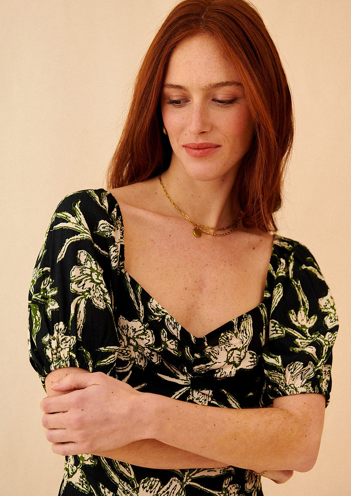 A woman wearing a sweetheart neck printed dress in black with cream and green floral print.