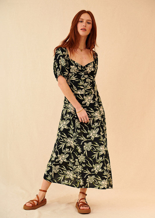 A woman wearing a sweetheart neck printed dress in black with cream and green floral print.