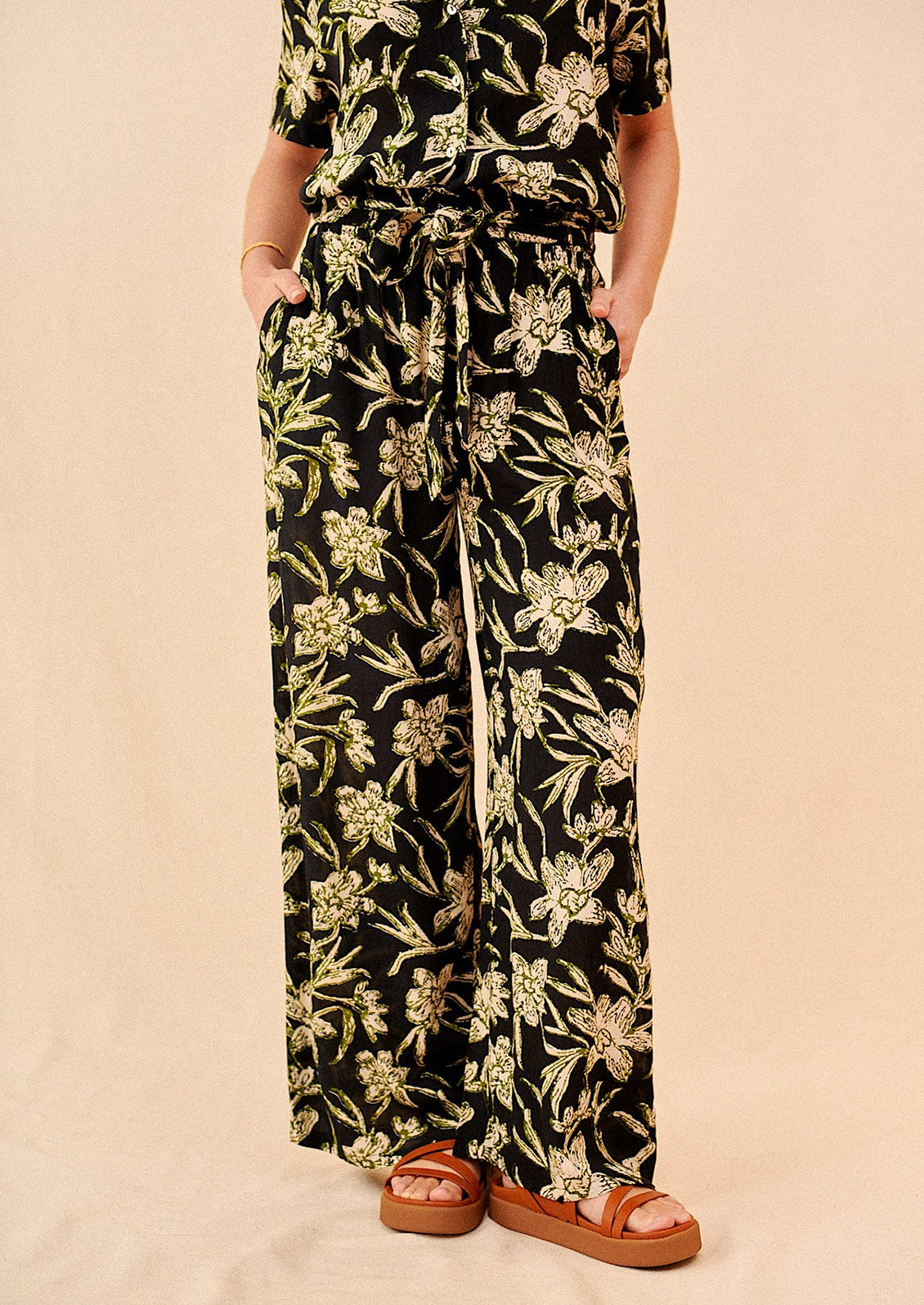 A pair of flowy pants in black with all over cream and green floral print.