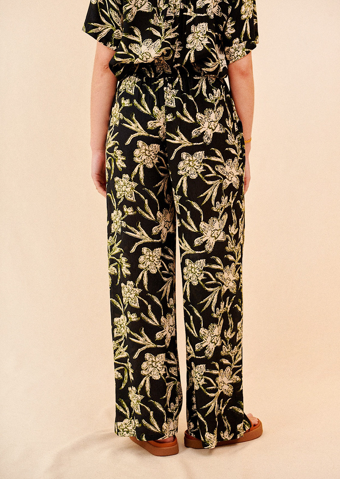 A pair of flowy pants in black with all over cream and green floral print.