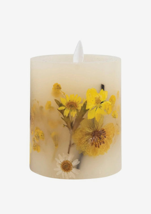 A natural wax pillar candle with embedded dried flowers.