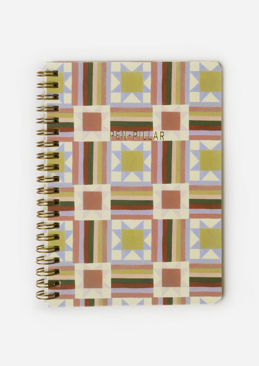 A spiral bound notebook with quilt illustrated cover.