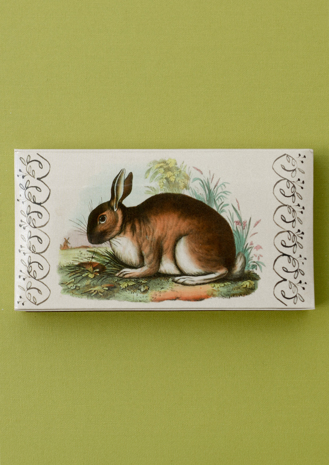 A matchbox with imagery of black rabbit, holding green tipped matches.