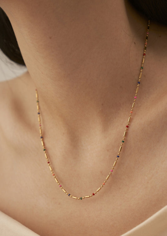 A woman wearing a gold chain necklace with small rainbow gradient stations.