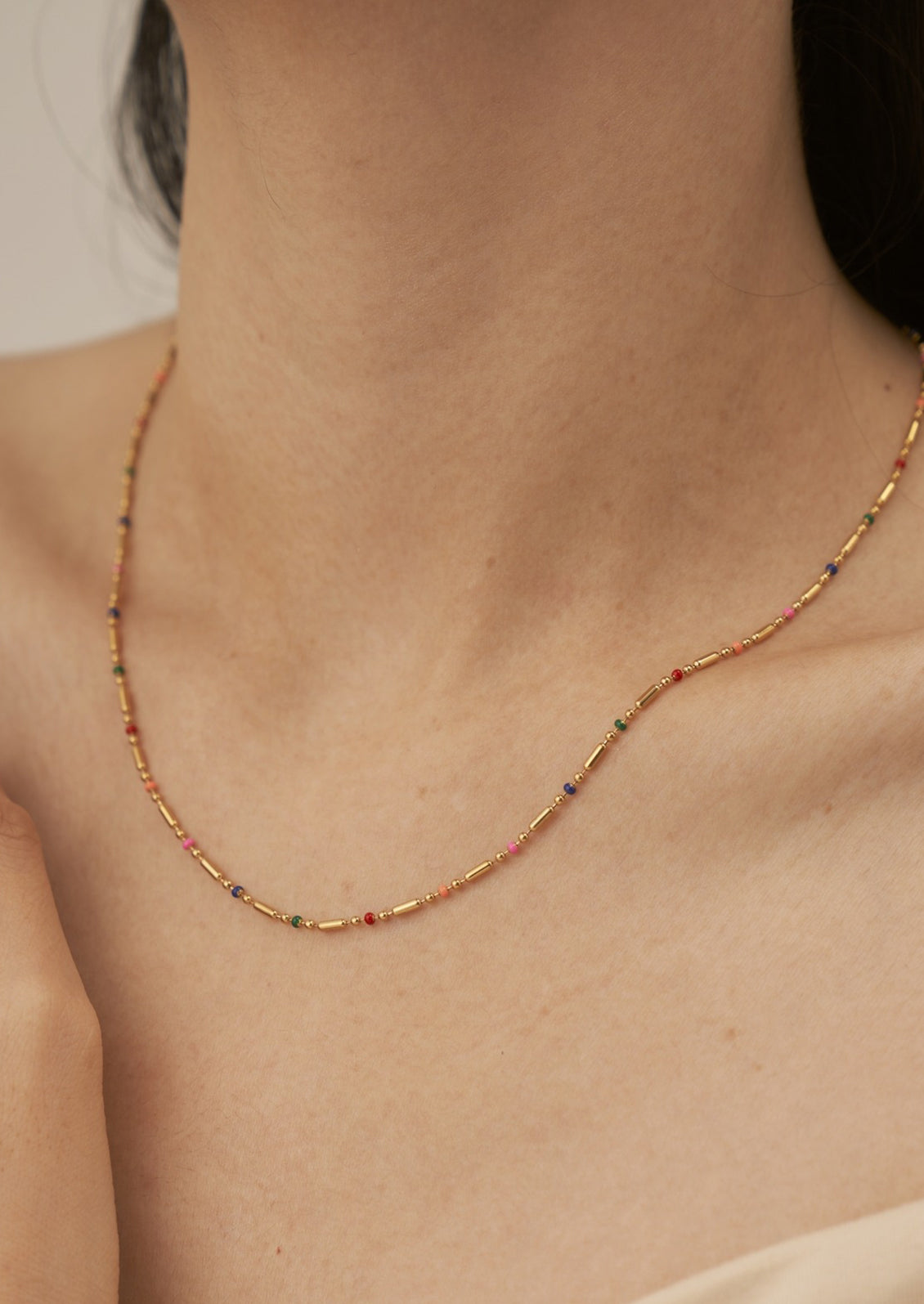 A woman wearing a gold chain necklace with small rainbow gradient stations.