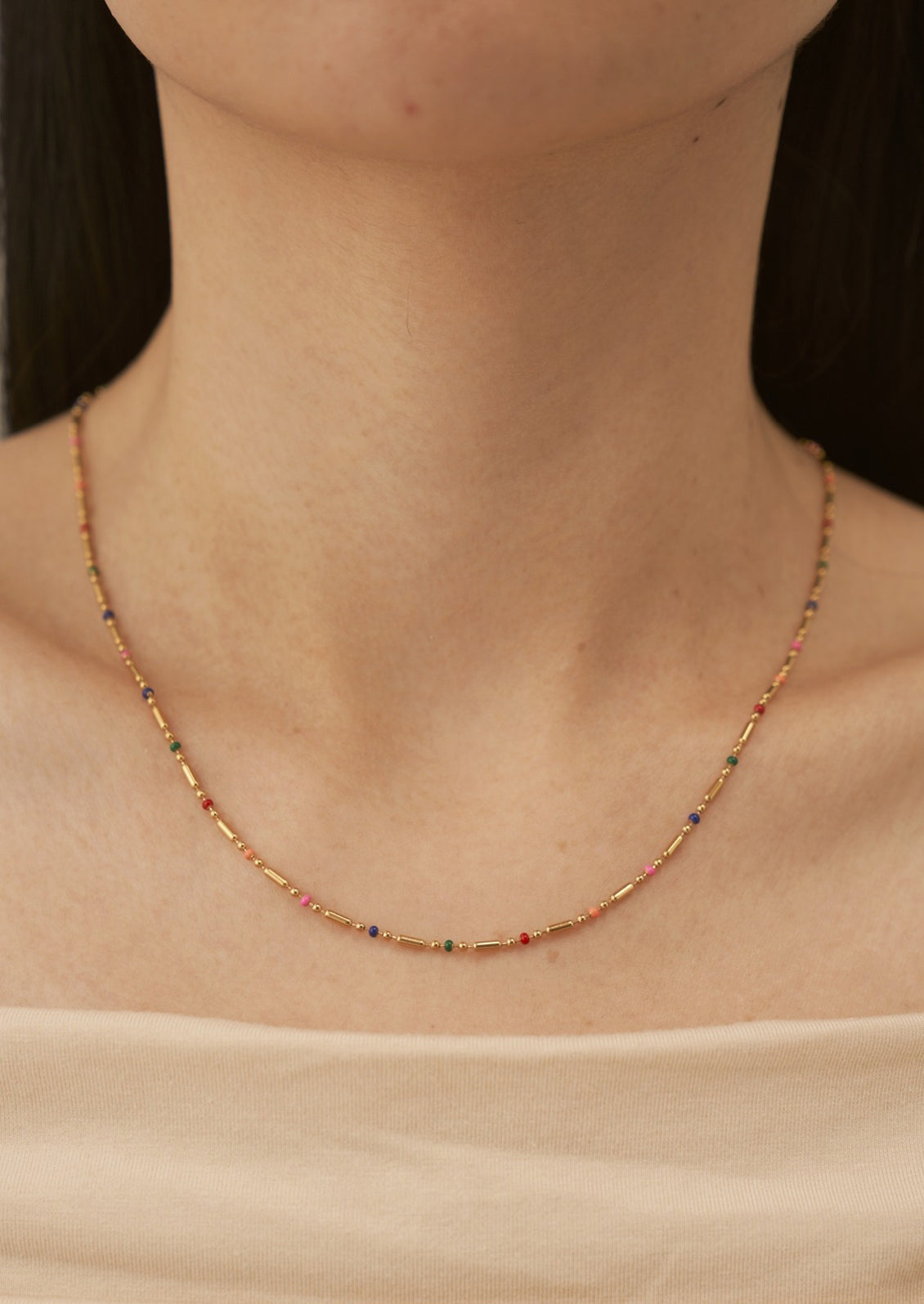 A woman wearing a gold chain necklace with small rainbow gradient stations.