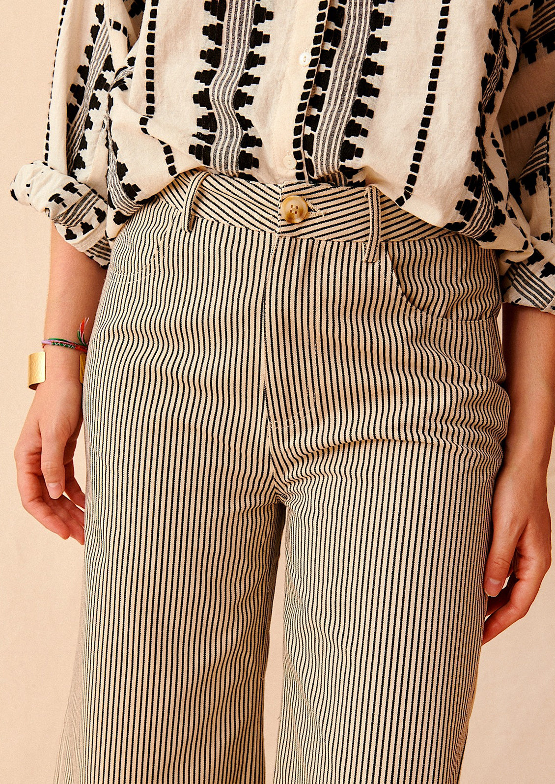 A woman wearing cream and black pinstriped jeans with detail of front