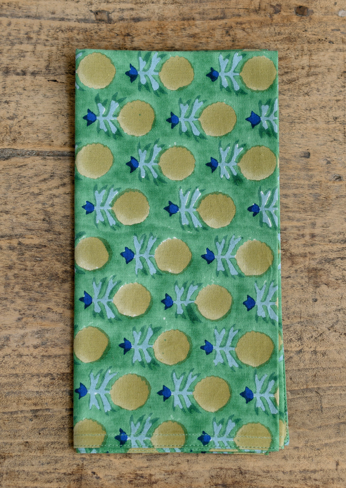 A green napkin with yellow and blue block printed floral pattern.