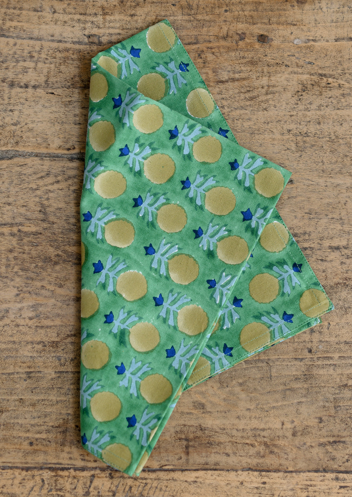 A green napkin with yellow and blue block printed floral pattern.