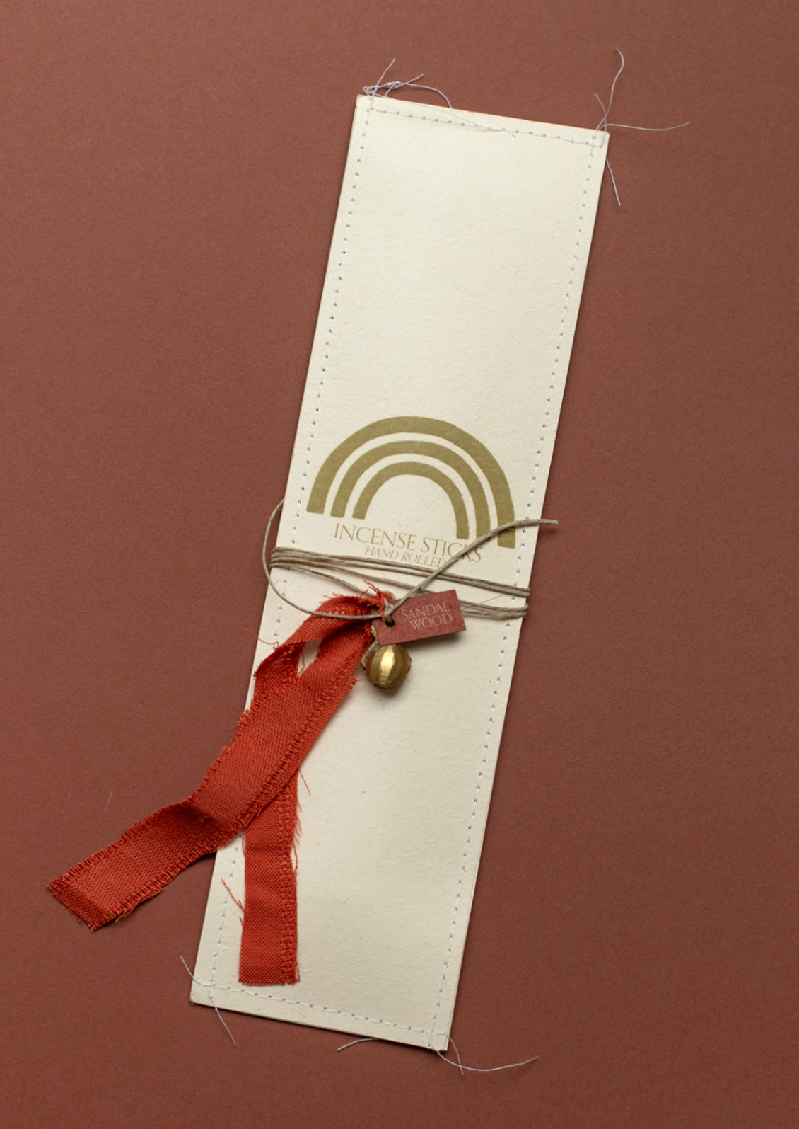 A pack of incense with red silk ribbon and brass charm, in sandalwood scent.