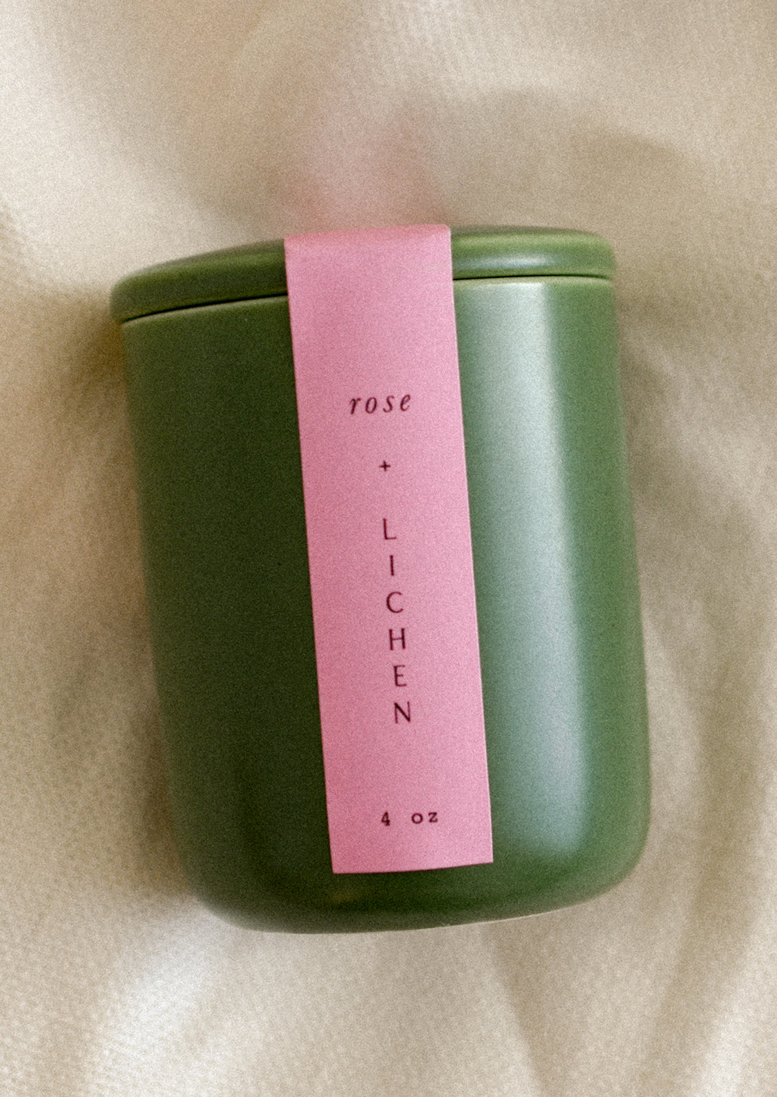 A small candle in lidded green ceramic jar in Rose and Lichen scent.