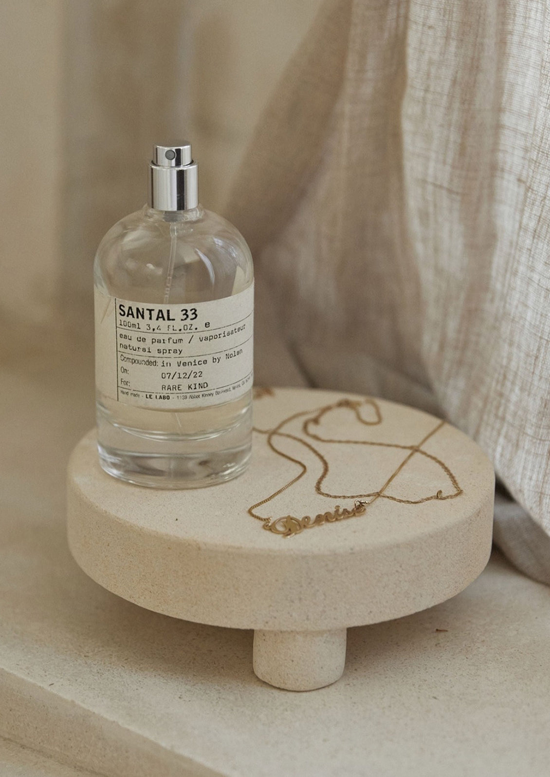 A tan sandstone round riser displaying perfume and jewelry.