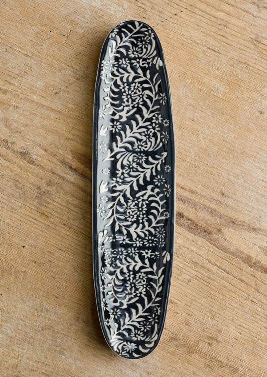 A slim, oval shaped ceramic tray in black with white botanical pattern.