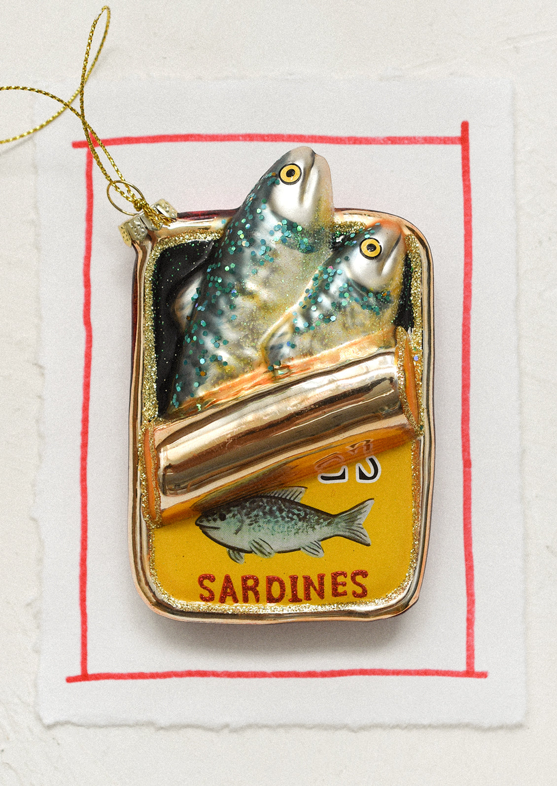 A glass holiday ornament in the shape of sardine tin with sardines coming out.