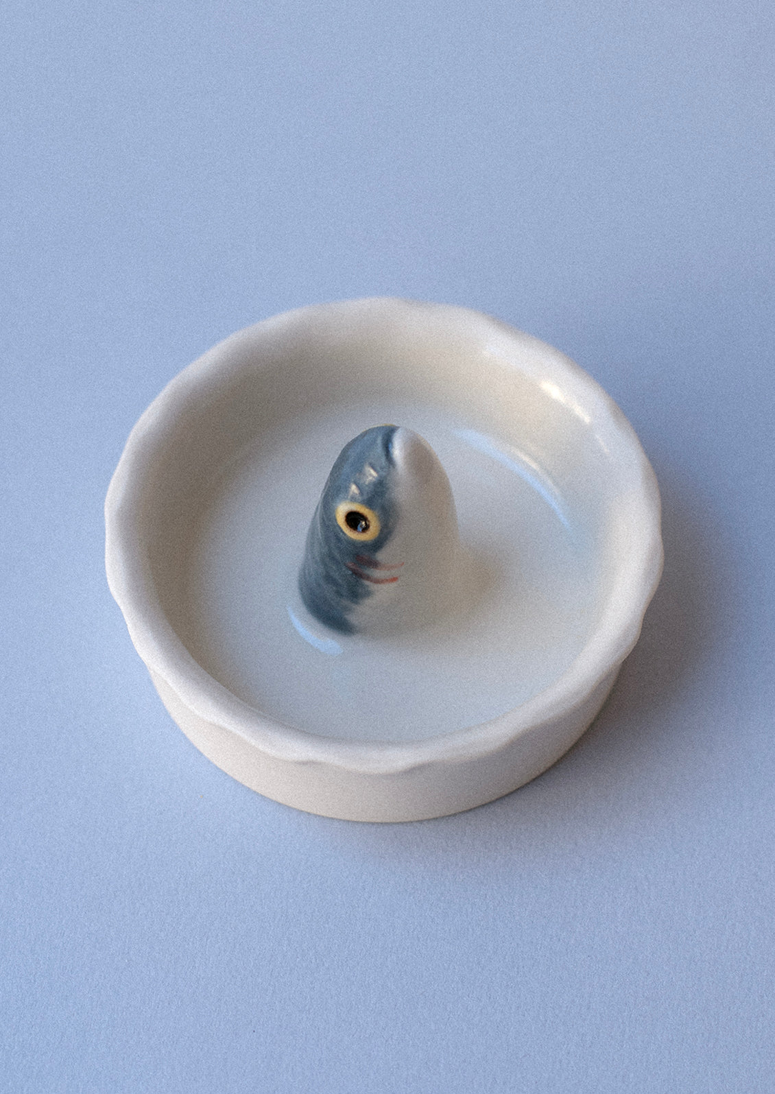 A round, white porcelain salt bowl with fish head sticking out from middle.