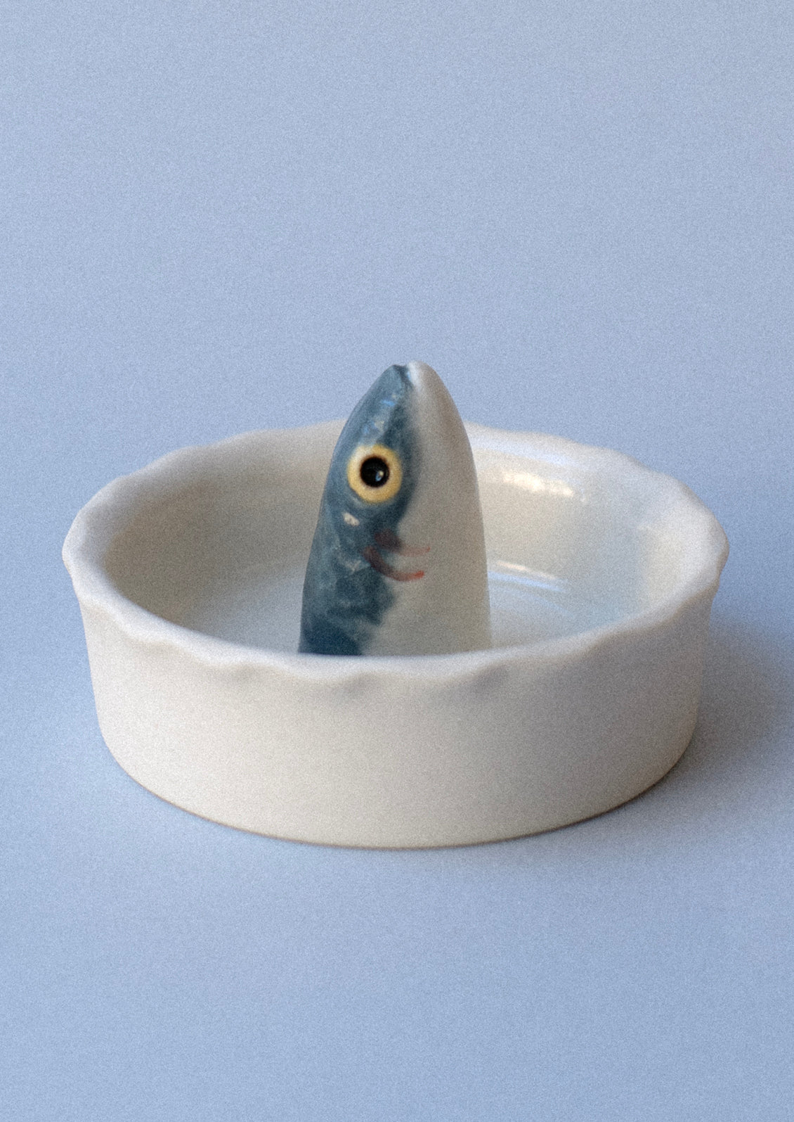 A round, white porcelain salt bowl with fish head sticking out from middle.