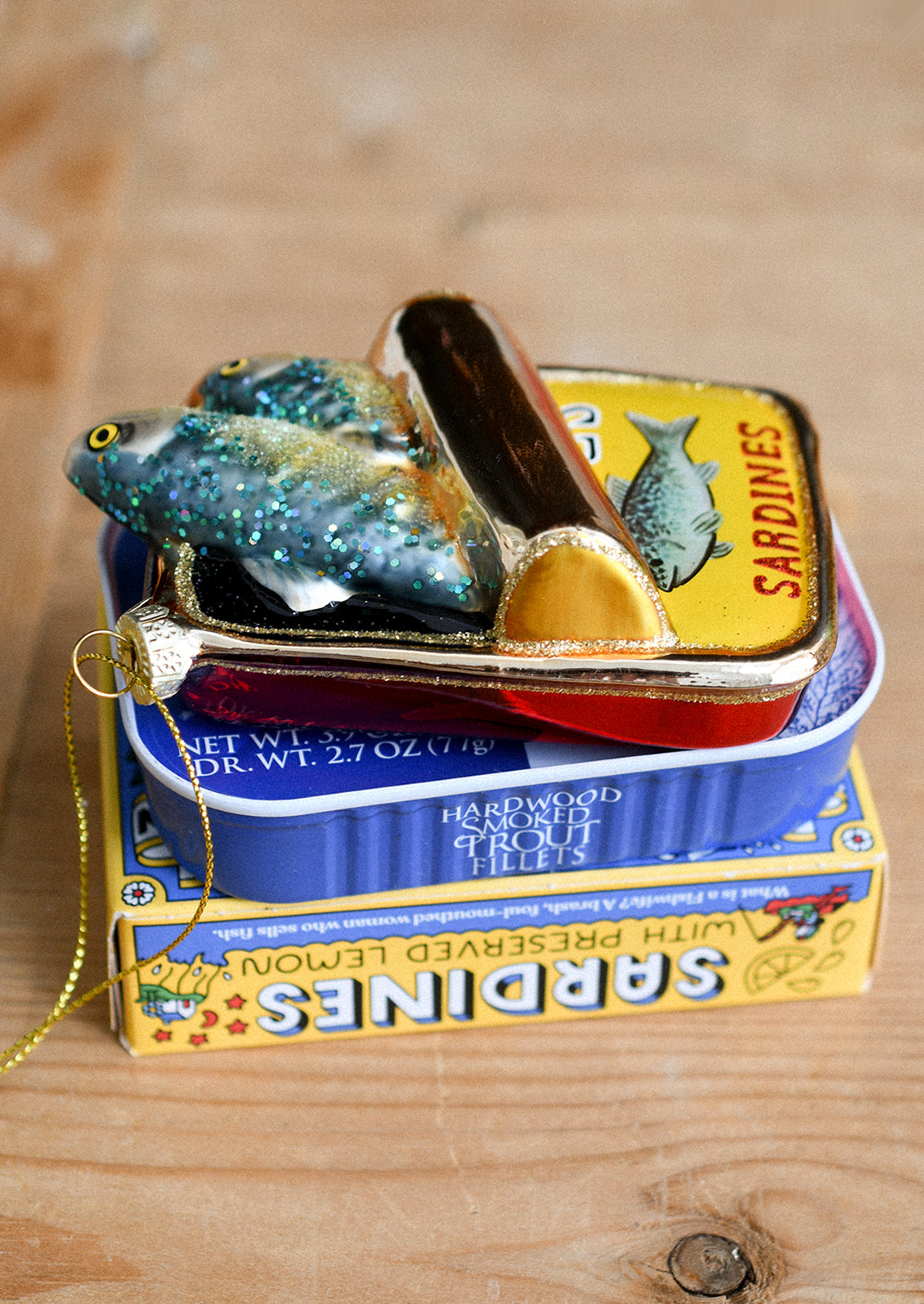 A glass holiday ornament in the shape of sardine tin with sardines coming out.