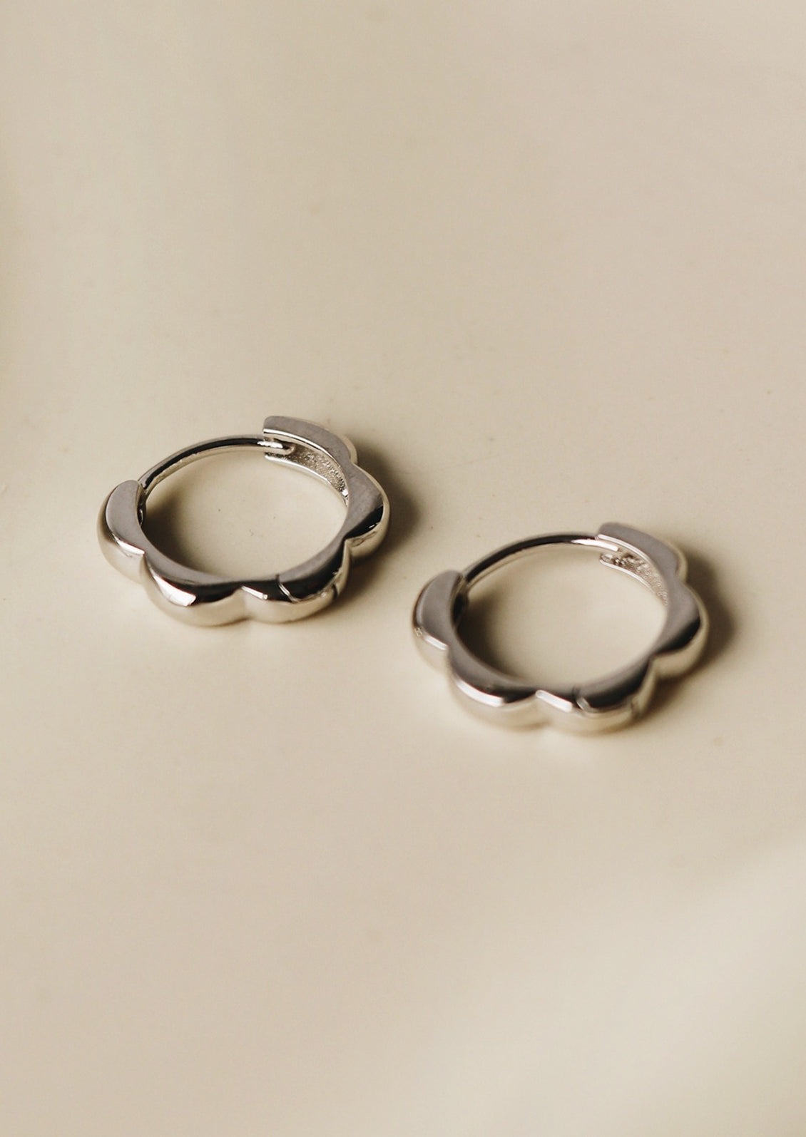 A pair of sterling silver huggie hoops with scalloped shape.