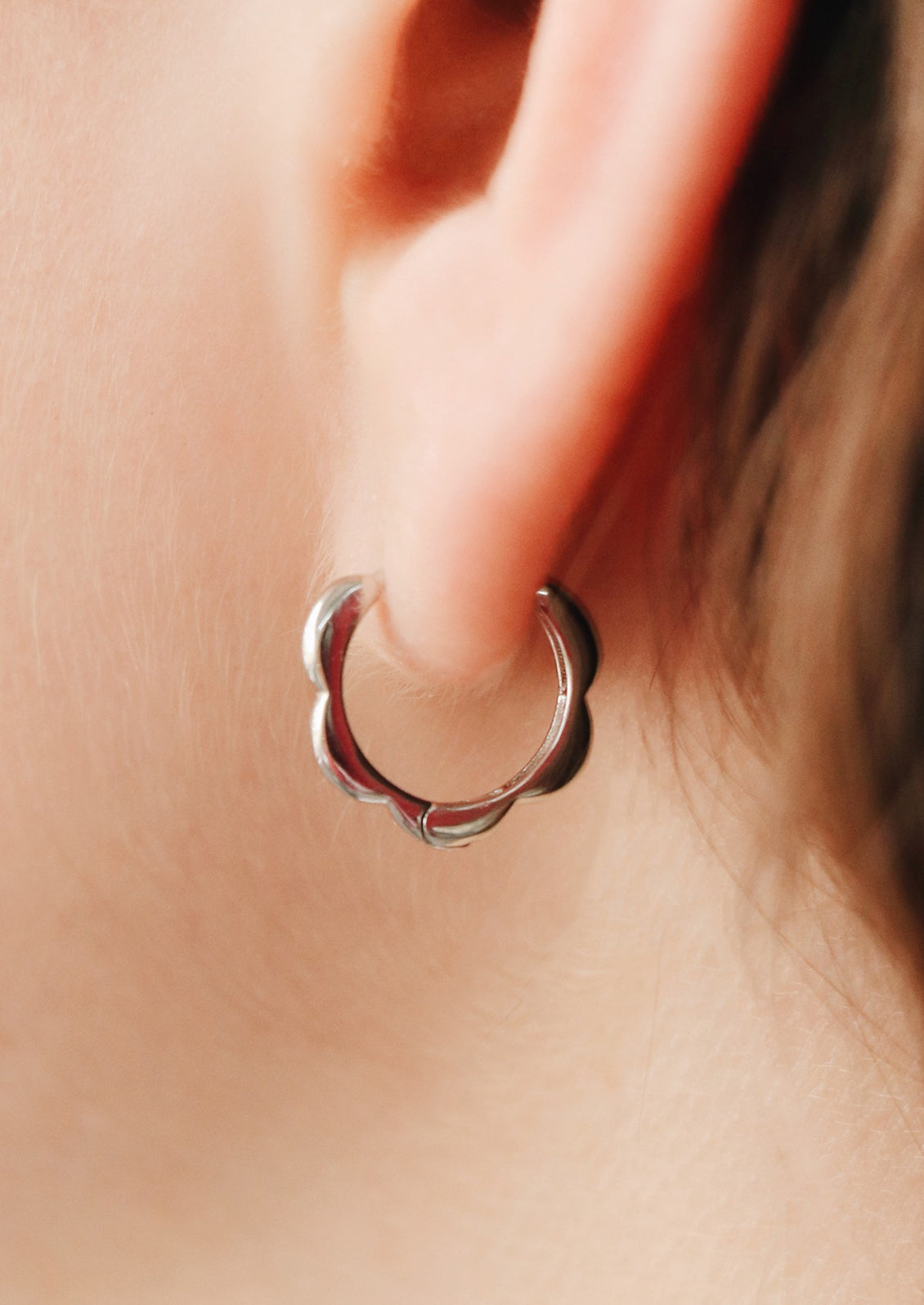 A pair of sterling silver huggie hoops with scalloped shape.